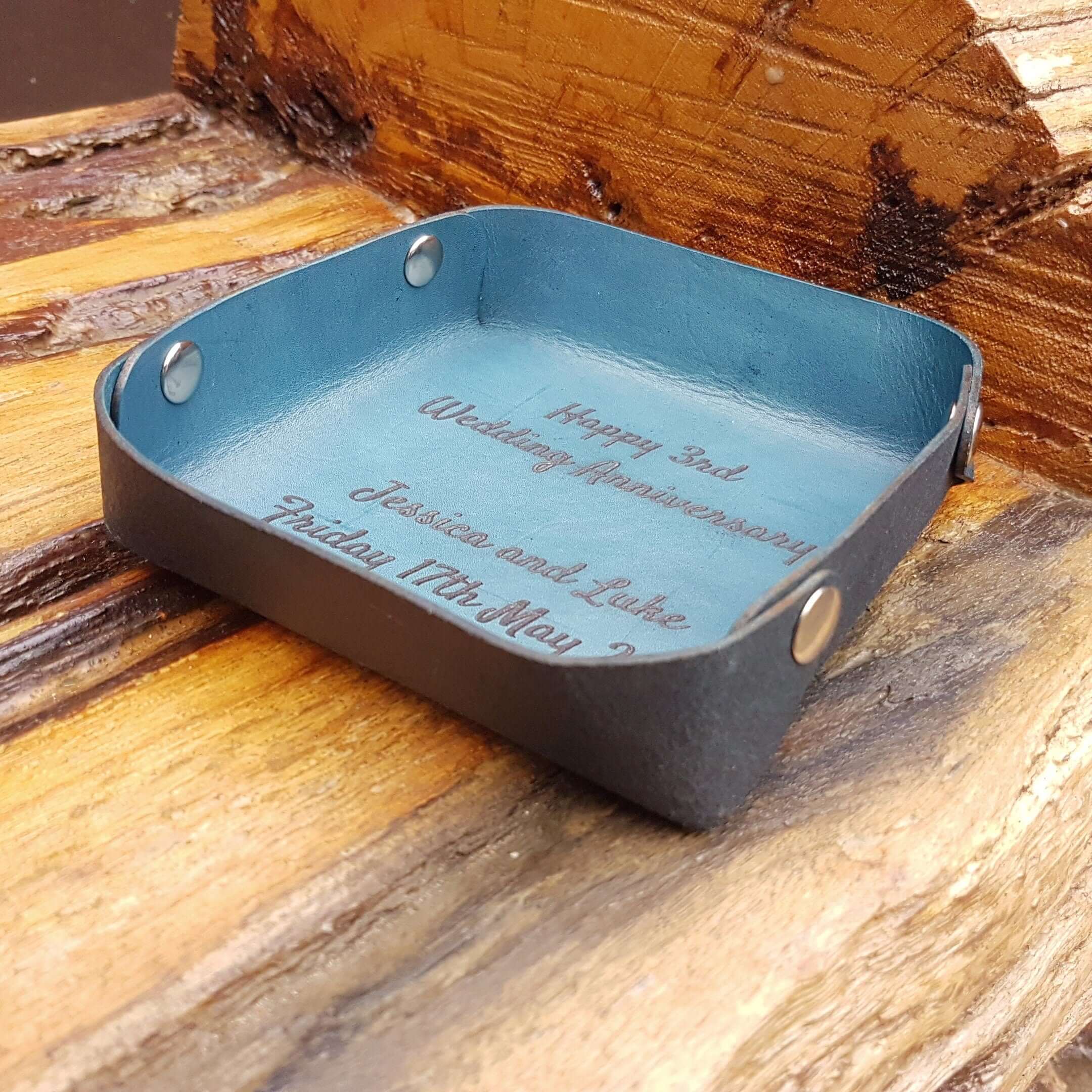 Personalized leather valet tray with engraved message for anniversary on a wooden surface.
